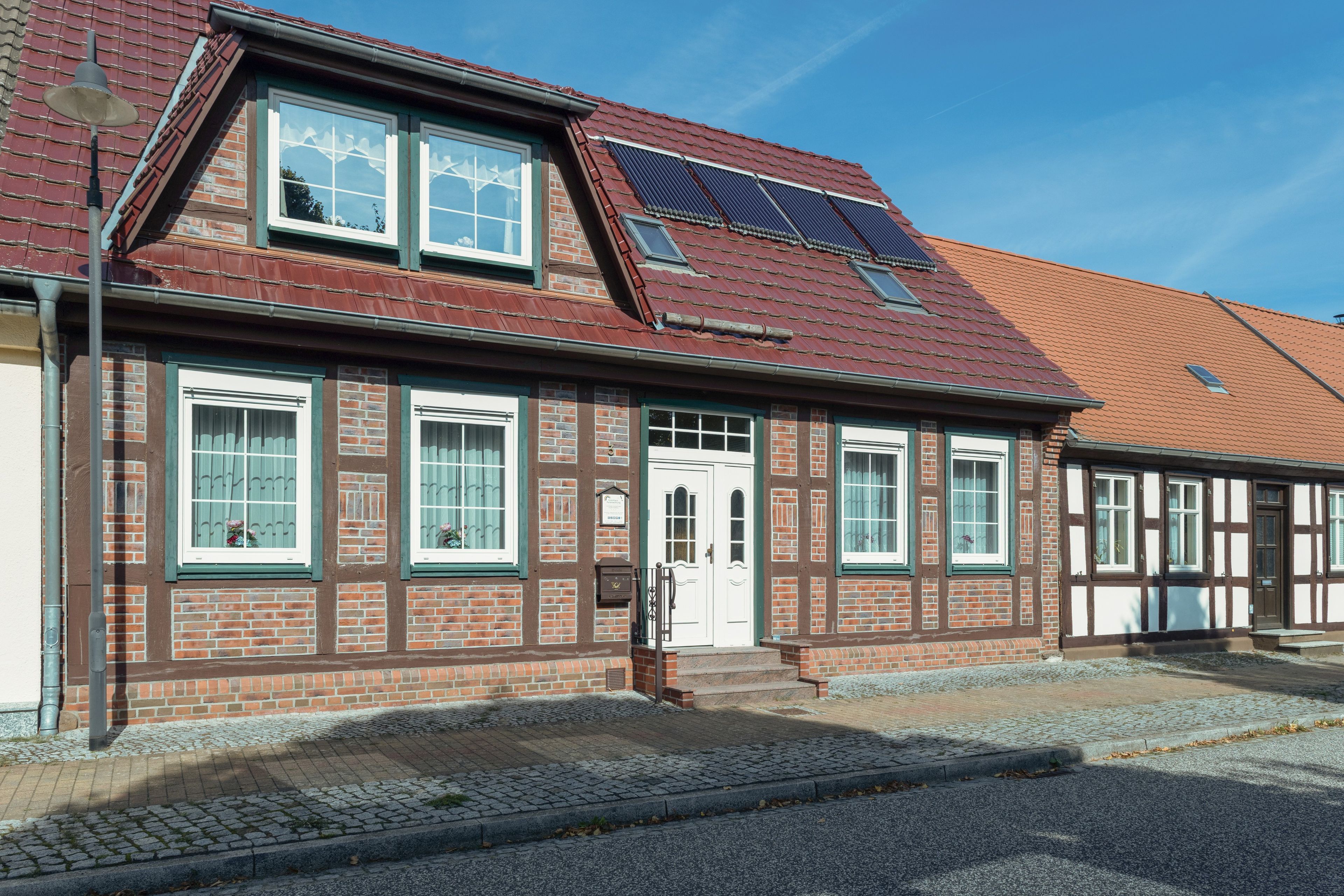 Ein traditionelles Fachwerkhäuschen mit geneigtem Dach, Solaranlagen und einer Kopfsteinpflasterauffahrt.