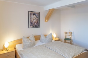 Ein Schlafzimmer mit einem Bett, zwei Nachttischen mit Lampen, einem Holzstuhl und einem Bild an der Wand.