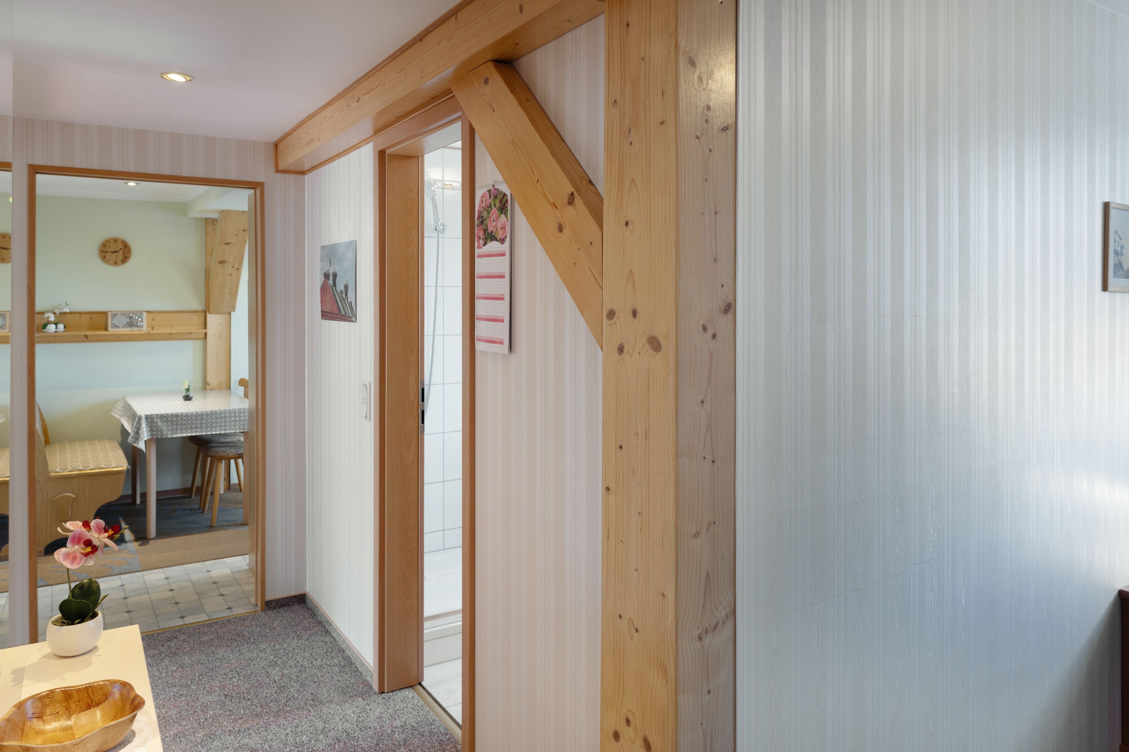 Ein Zimmer mit Holzbalken an der Decke, einem Essbereich mit Tisch und Stühlen sowie einer Tür zu einem anderen Raum.