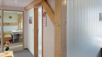 Ein Zimmer mit Holzbalken an der Decke, einem Essbereich mit Tisch und Stühlen sowie einer Tür zu einem anderen Raum.