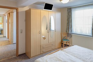 Un dormitorio con cama, armario, silla y ventana con cortinas.