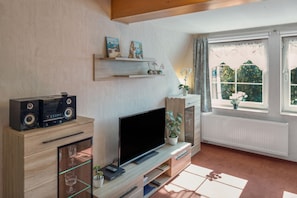 Ein modernes Wohnzimmer mit Flachbildfernseher, einer Holzunterhaltungsecke und einem großen Fenster mit Vorhängen.