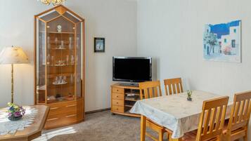 Ein Essbereich mit Tisch, Stühlen, einem Fernseher, einer Vitrine mit Glaswaren und einem Gemälde an der Wand.