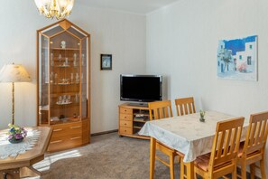 Un comedor con una mesa, sillas, un televisor, un mueble con cristalería y un cuadro en la pared.
