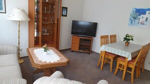A living room with a sofa, a table with a lace tablecloth, a TV on a wooden stand, a cabinet with glass doors, and a painting on the wall. - Apartment 'Für 2 Personen 45 M²' with Private Terrace and Wi-Fi (Bad Wilsnack)