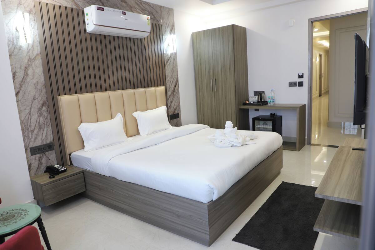 Una habitación de hotel moderna con una cama grande, una mesita de noche con teléfono, una pequeña mesa con silla y un armario.