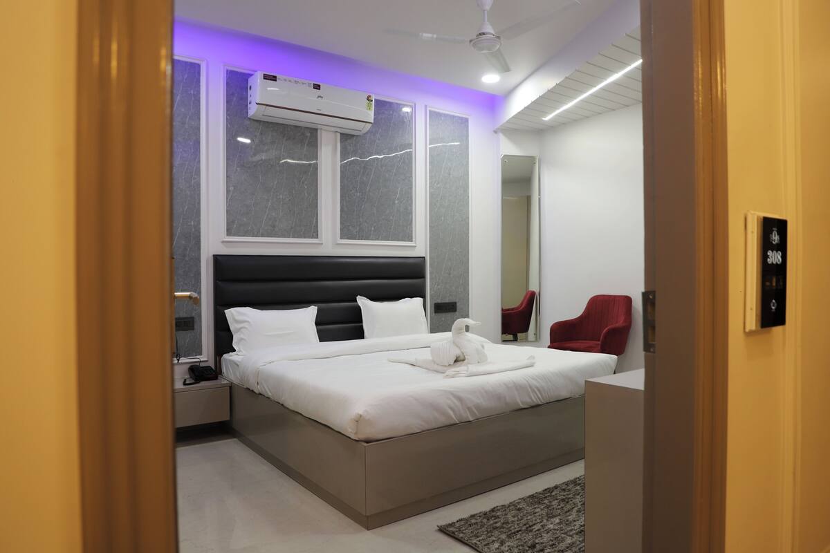 Una habitación de hotel moderna con una cama grande, una mesita de noche, una silla roja y un equipo de aire acondicionado.