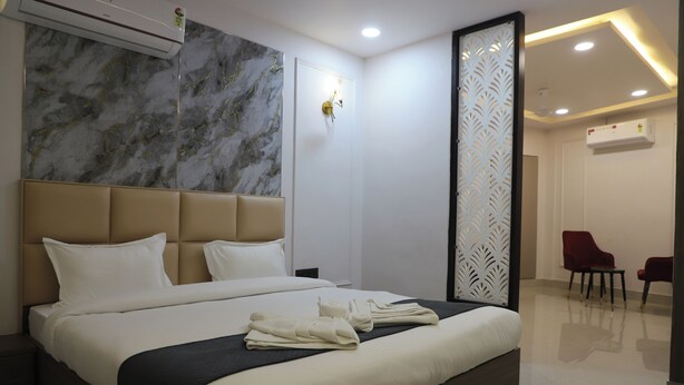 Habitació d'hotel moderna amb un llit gran, una paret de marbre, un aparell d'aire condicionat i una zona de seients amb dues cadires.