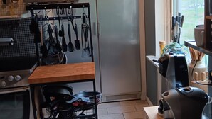 A kitchen with a stainless steel refrigerator, microwave, oven, and a utensil rack.