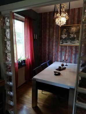 Un comedor con una mesa, sillas, una araña y una ventana con cortinas.