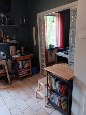 A room with a kitchen area, a bookshelf, a small table, and a window with a view of greenery. - Room-room in Apartment Within Walking di (Gothenburg)