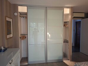 A bedroom with a sliding glass door closet, a bedside table, and a bed. - Paradis d'Azur: 1-bedroom apt facing the sea, a/c (Menton)