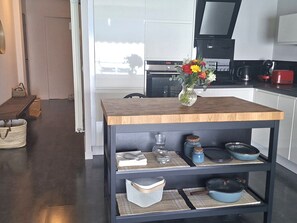 A modern kitchen with a wooden table, shelves with kitchenware, and a vase with flowers. - Paradis d'Azur: 1-bedroom apt facing the sea, a/c (Menton)
