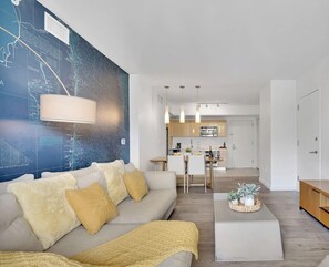 Ett modernt vardagsrum med en soffa, ett soffbord och en tv. Längre in i rummet finns ett kök med en matplats.