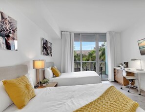 Une chambre d’hôtel avec deux lits, un bureau, une chaise, une télévision et un balcon avec vue.