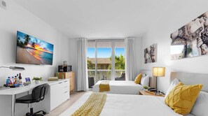 A hotel room with a bed, a desk, a chair, a TV, and a window with a view of palm trees. - Beachwalk Resort · 2BR · Intracoastal View (Hallandale Beach)