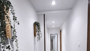 A hallway with white textured walls, a wooden floor, and hanging plants.
