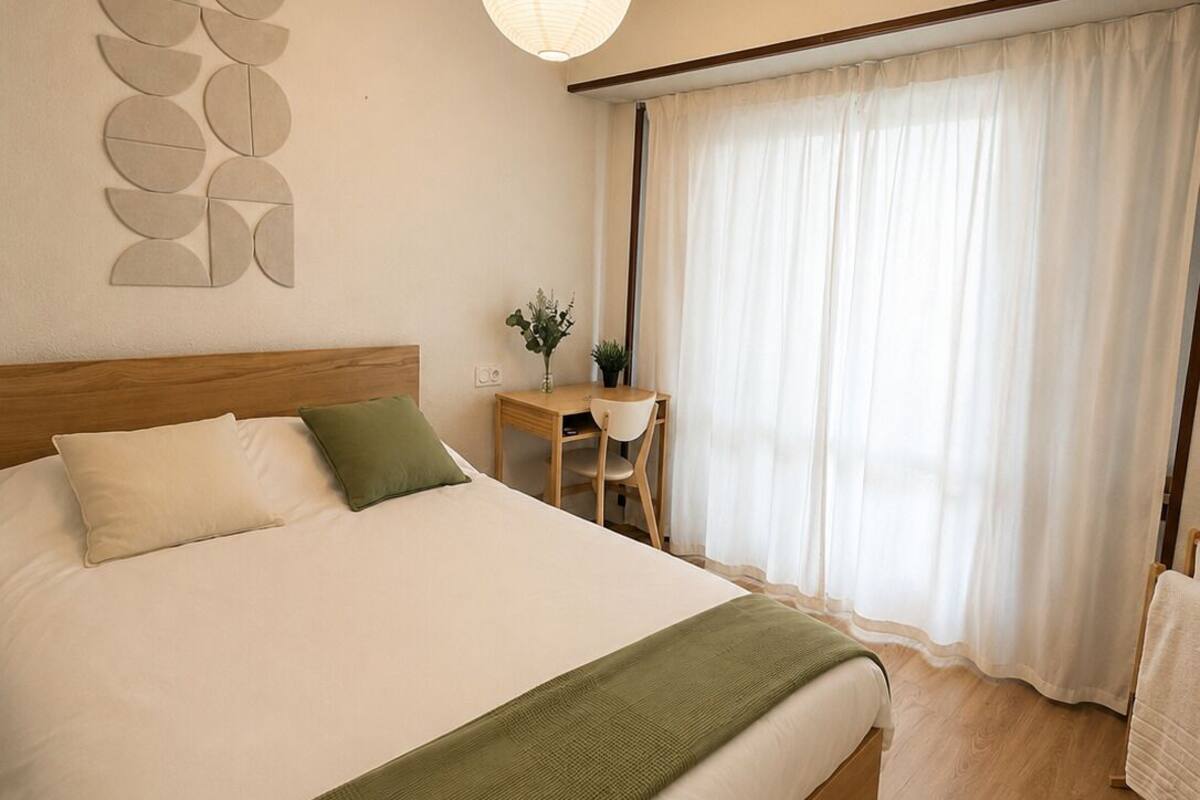 A neatly arranged bedroom with a bed, a desk, and a window with curtains.