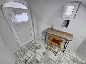 Et værelse med en hvid dør, et lille bord med en stol, et vindue og et gulv med et mønster.