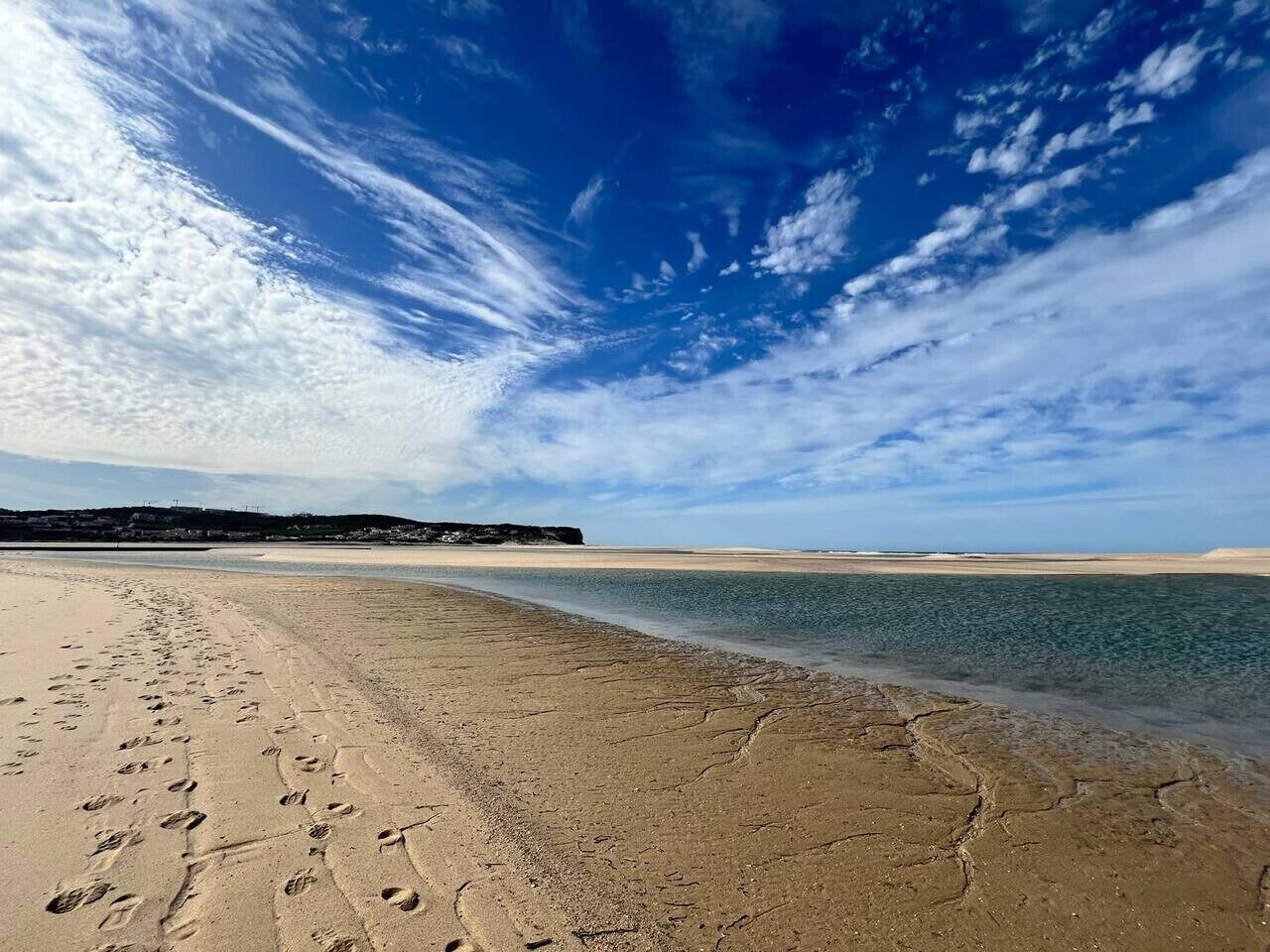 Une plage parsemée d’empreintes, un ciel dégagé et une côte lointaine.