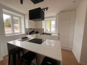 Una cocina moderna con una isla grande, muebles blancos y una campana extractora negra.