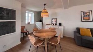 A modern living room with a round wooden dining table, wicker chairs, a grey sofa with a mustard-colored pillow, a white cabinet, and a hanging pendant light. - Cozy getaway at Obidos lagoon & ocean (Foz do Arelho)