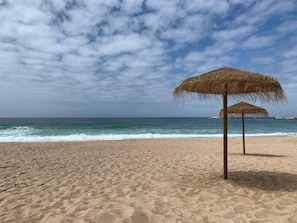 Ein Strand mit einem Strohdachschirm und ruhiger See.