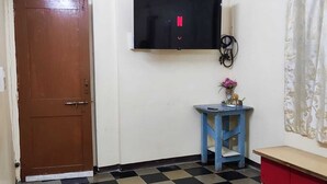 A room with a checkered floor, a brown door, a blue table, a red bench, a ceiling fan, and an air conditioning unit. - In Main market of Solapur (Solapur)