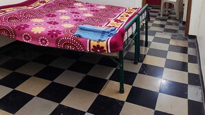 Una habitación con una cama, un ventanal, piso de cuadros y una puerta que da a otra habitación.