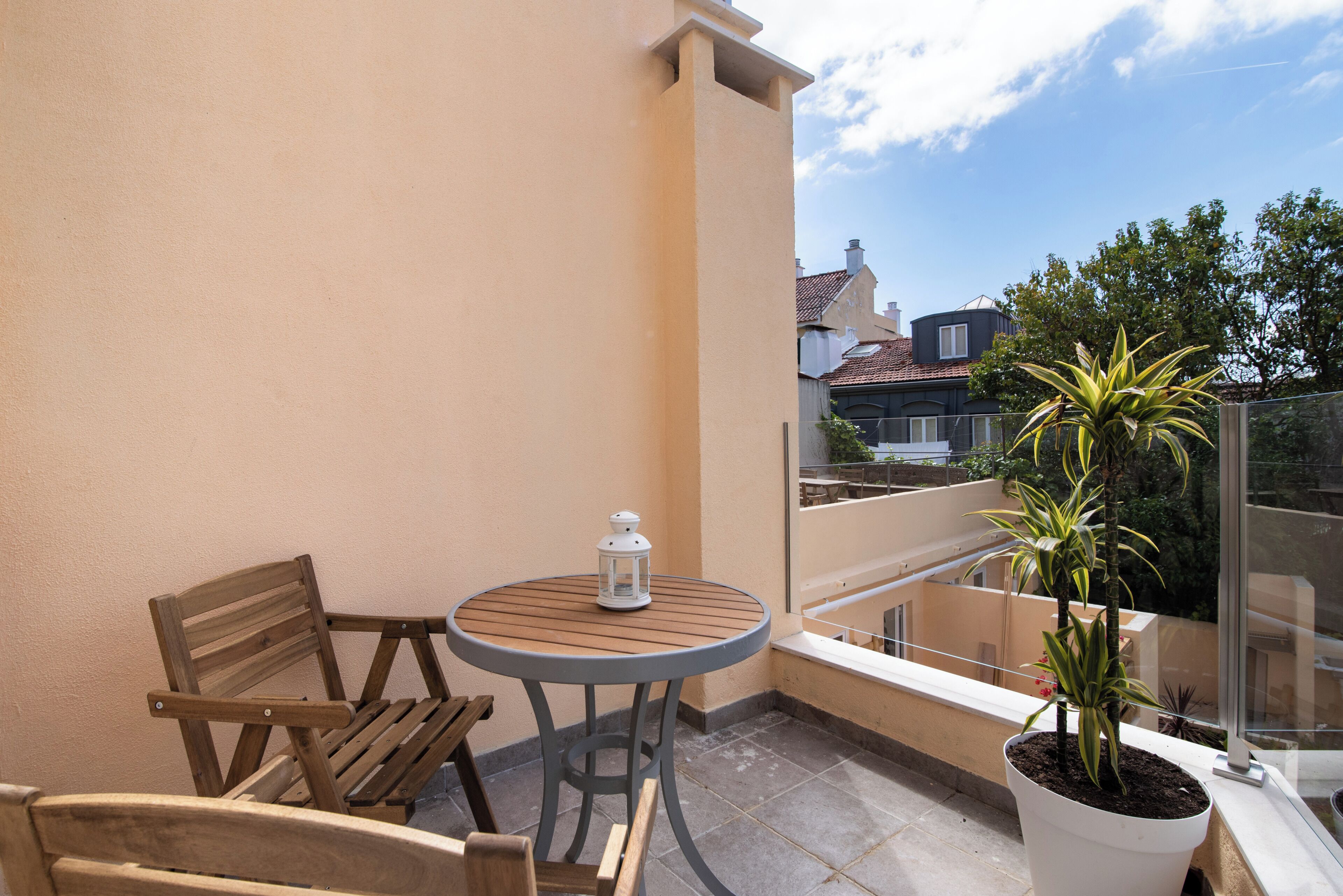 A balcony with a round table, two wooden chairs, a potted plant, and a white lantern.
