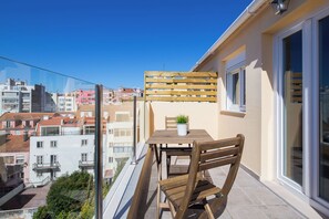Un balcón con mesa y sillas de madera, una planta en maceta y vistas de la ciudad.