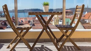 A balcony with a wooden table and chairs, a potted plant, and a view of a cityscape. - Designer Flats in Lapa (Lisbon)