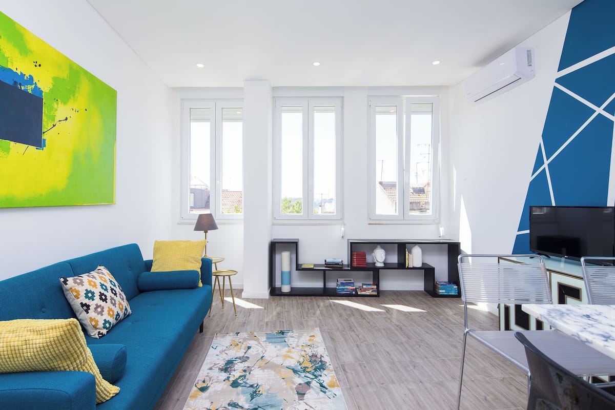 Un salon moderne avec un canapé bleu, un coussin décoratif à motifs, une table basse et un grand tableau abstrait accroché au mur.