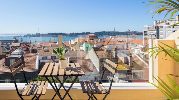 A balcony with a view of a coastal cityscape, including buildings with red-tiled roofs and a clear blue sky. - Designer Flats in Lapa (Lisbon)