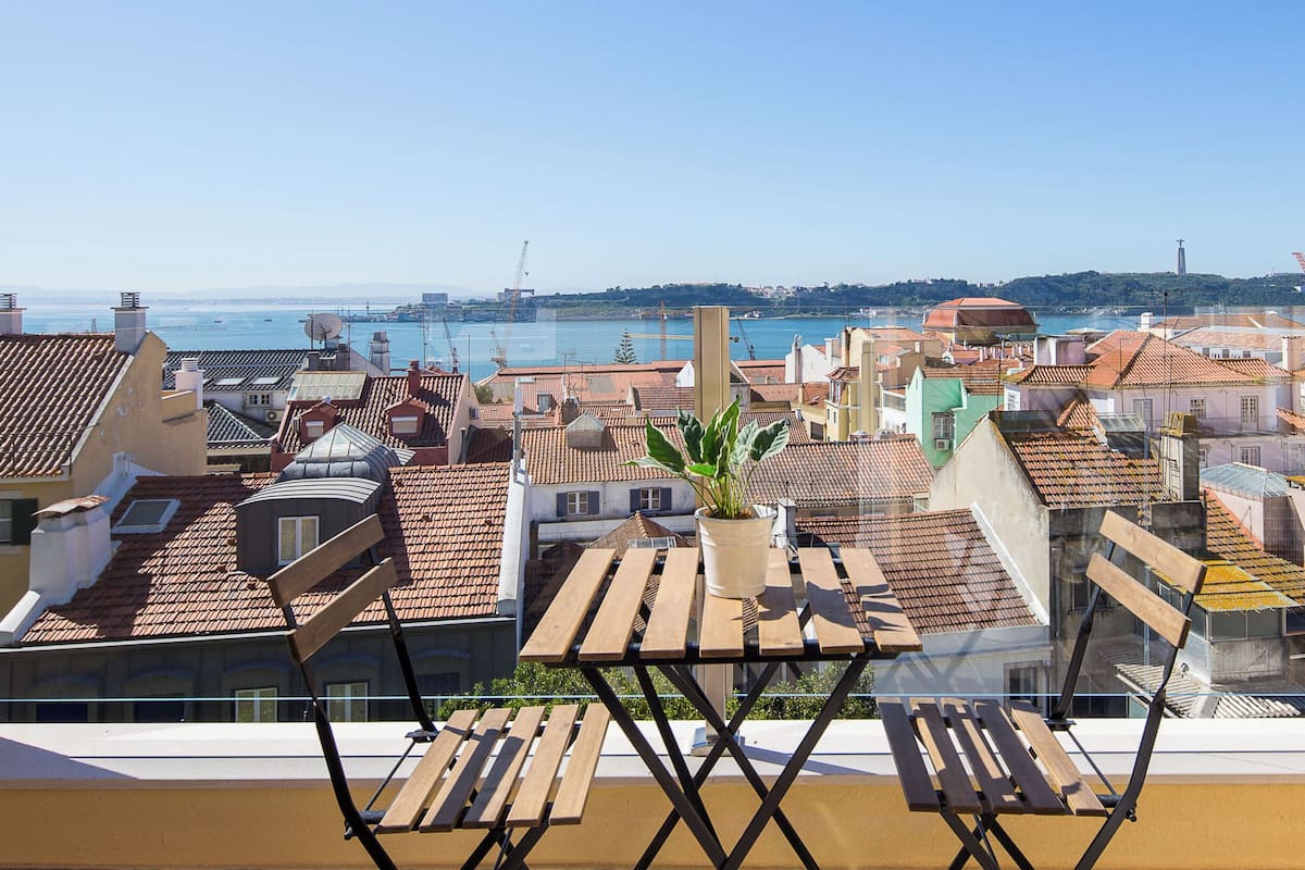 Un balcon offrant une vue sur le paysage urbain de la côte, avec des bâtiments aux toits recouverts de tuiles rouges et un ciel bleu dégagé.