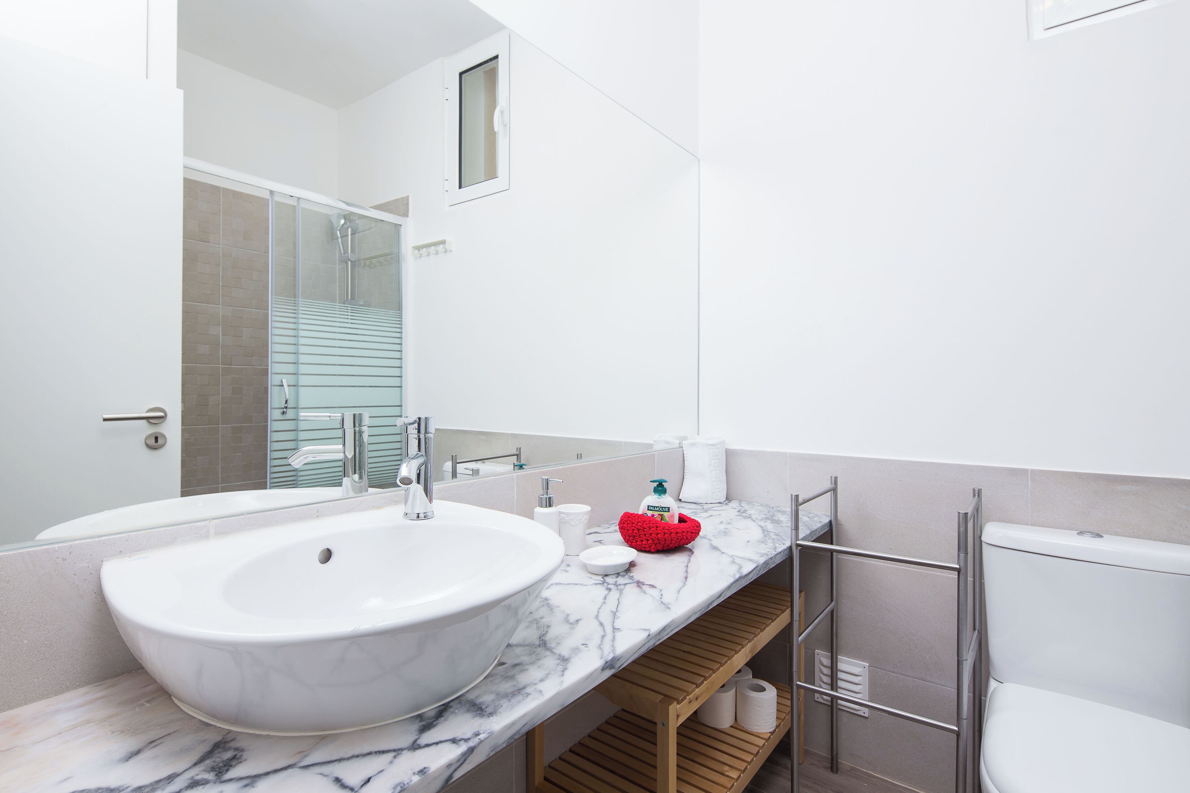 Une salle de bain moderne avec un grand lavabo blanc, une douche en verre et une étagère en bois.