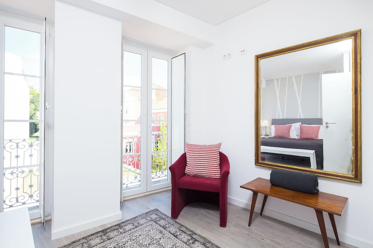 Une pièce avec un fauteuil rouge, un banc, un grand miroir et une vue sur l’extérieur, visible à travers une porte vitrée.