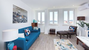 A living room with a blue sofa, a coffee table, a lamp, a painting on the wall, and large windows. - Designer Flats in Lapa (Lisbon)