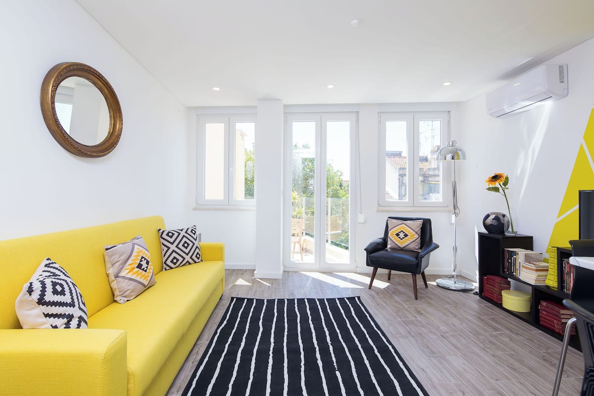Un salon lumineux avec un canapé jaune, un tapis rayé noir et blanc et un fauteuil noir.