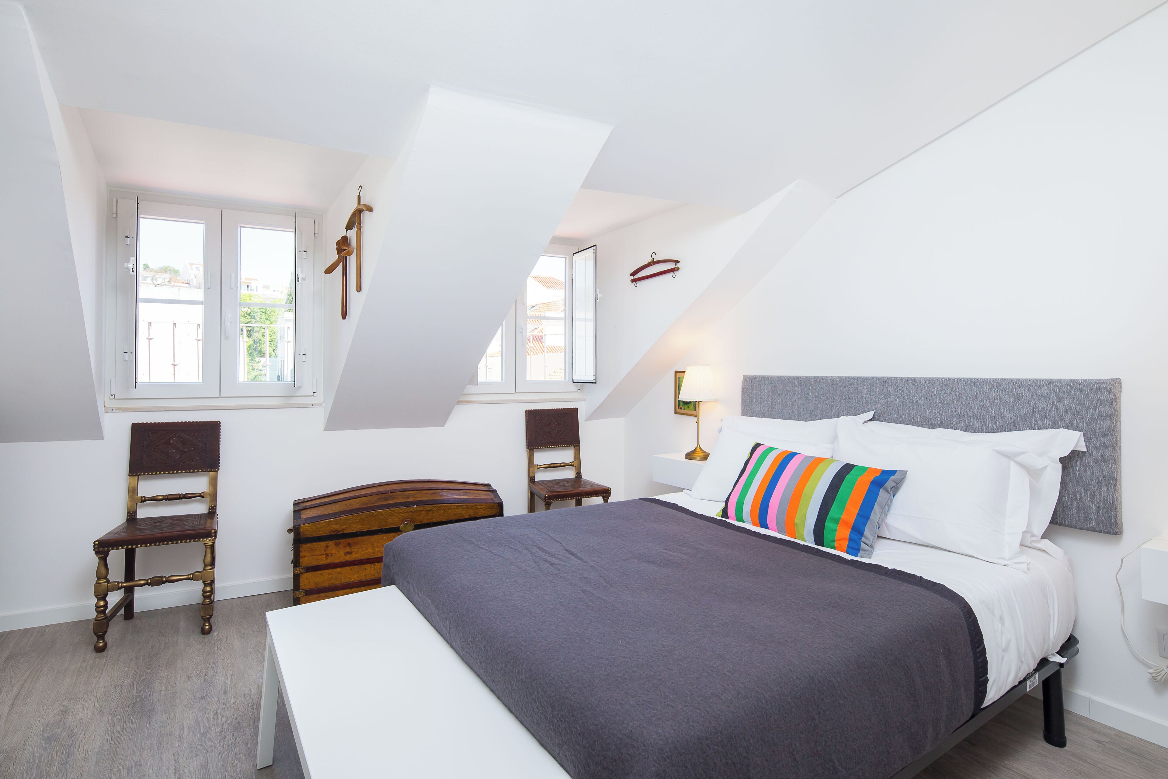 Ein Schlafzimmer mit einem Bett, zwei Stühlen, einer Kommode und einem Fenster.