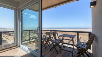 Un balcon avec vue sur la plage, des meubles en bois et une porte vitrée.