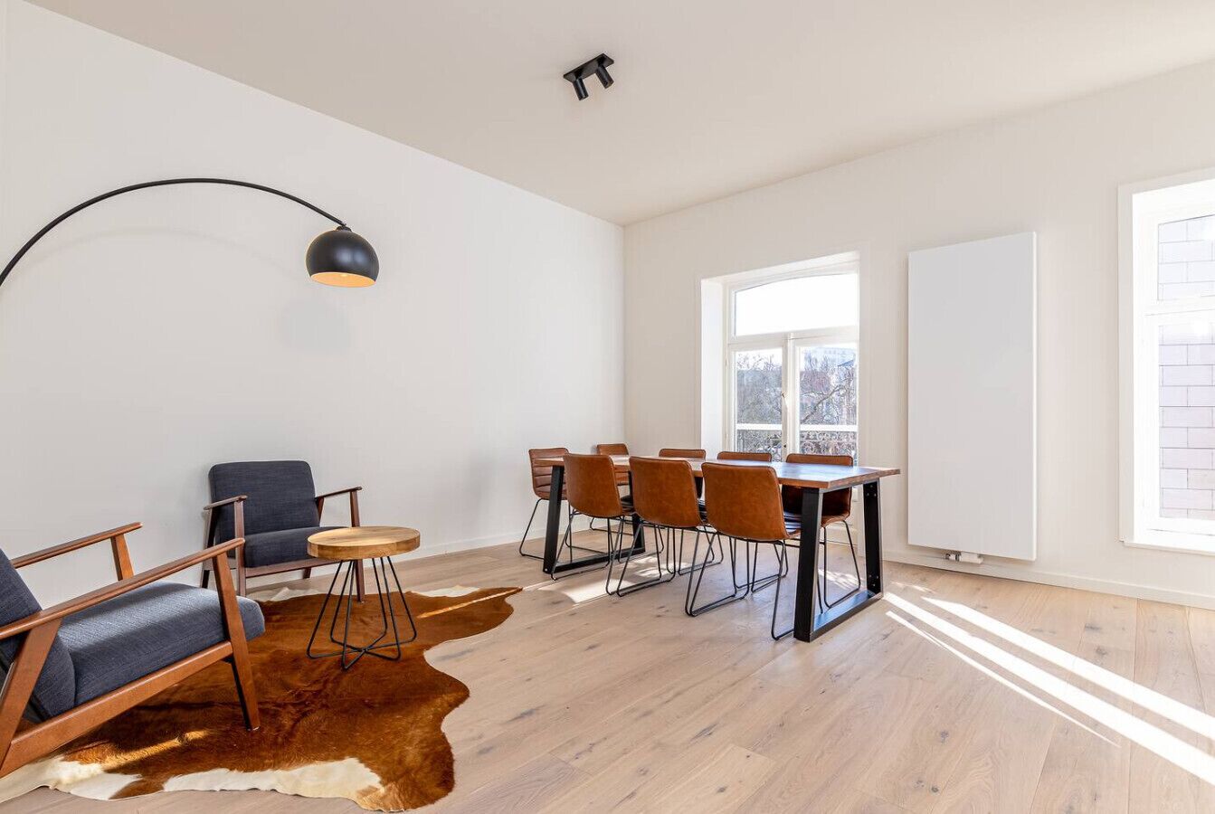 A spacious room with a dining table, chairs, a sofa, a lamp, and a large window.