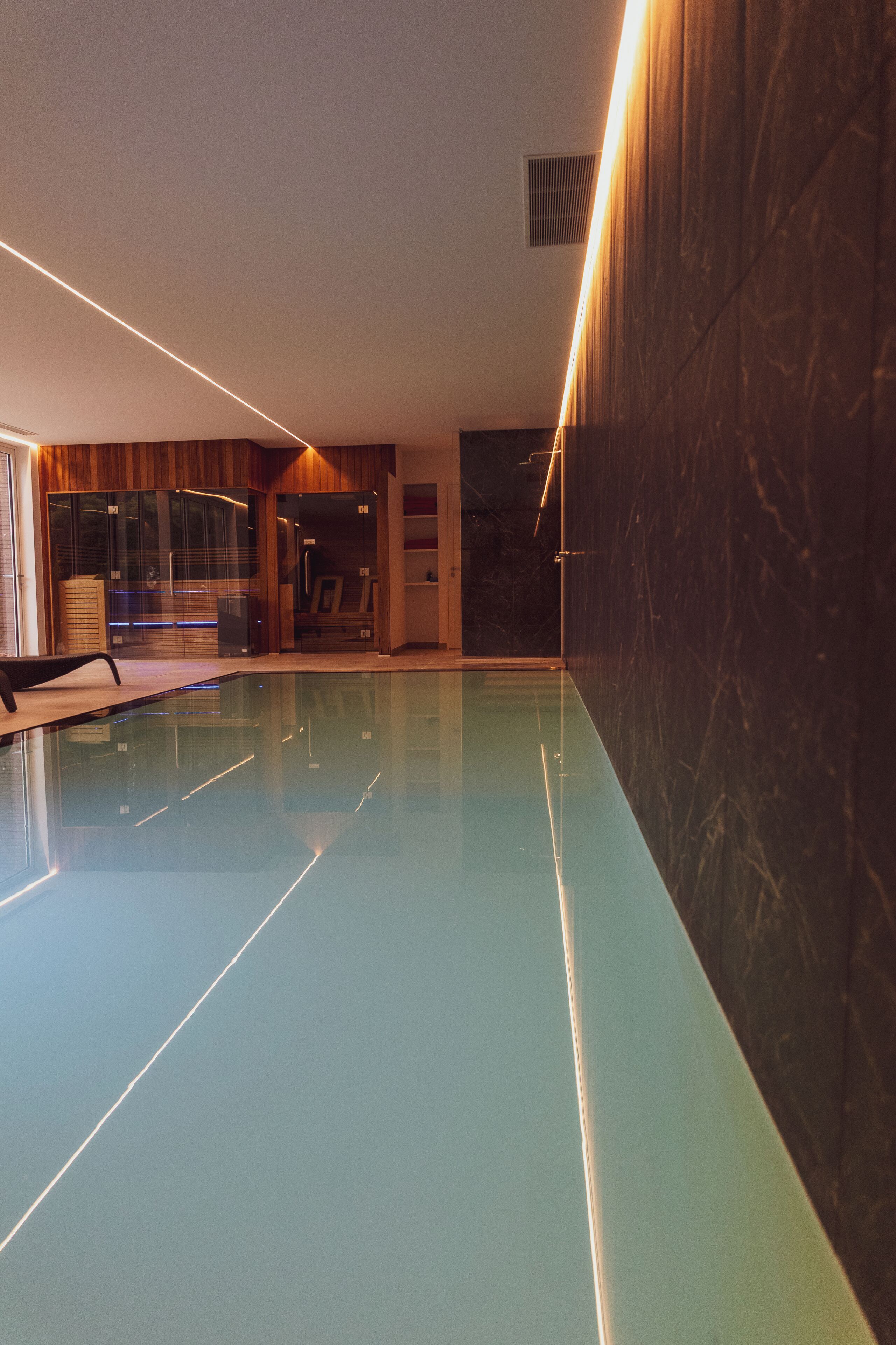 A swimming pool with a glass wall, wooden paneling, and a ceiling vent.