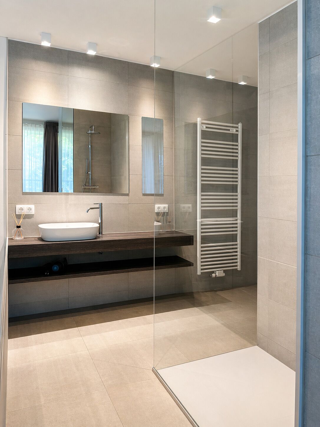 A modern bathroom with a glass shower enclosure, a white sink, and a towel rack.