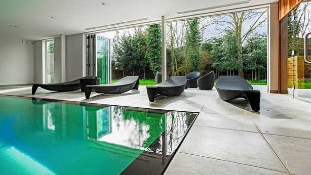 A modern indoor pool area with a clear view of the outdoors, including trees and a building. - Huyze Fox (Bruges)