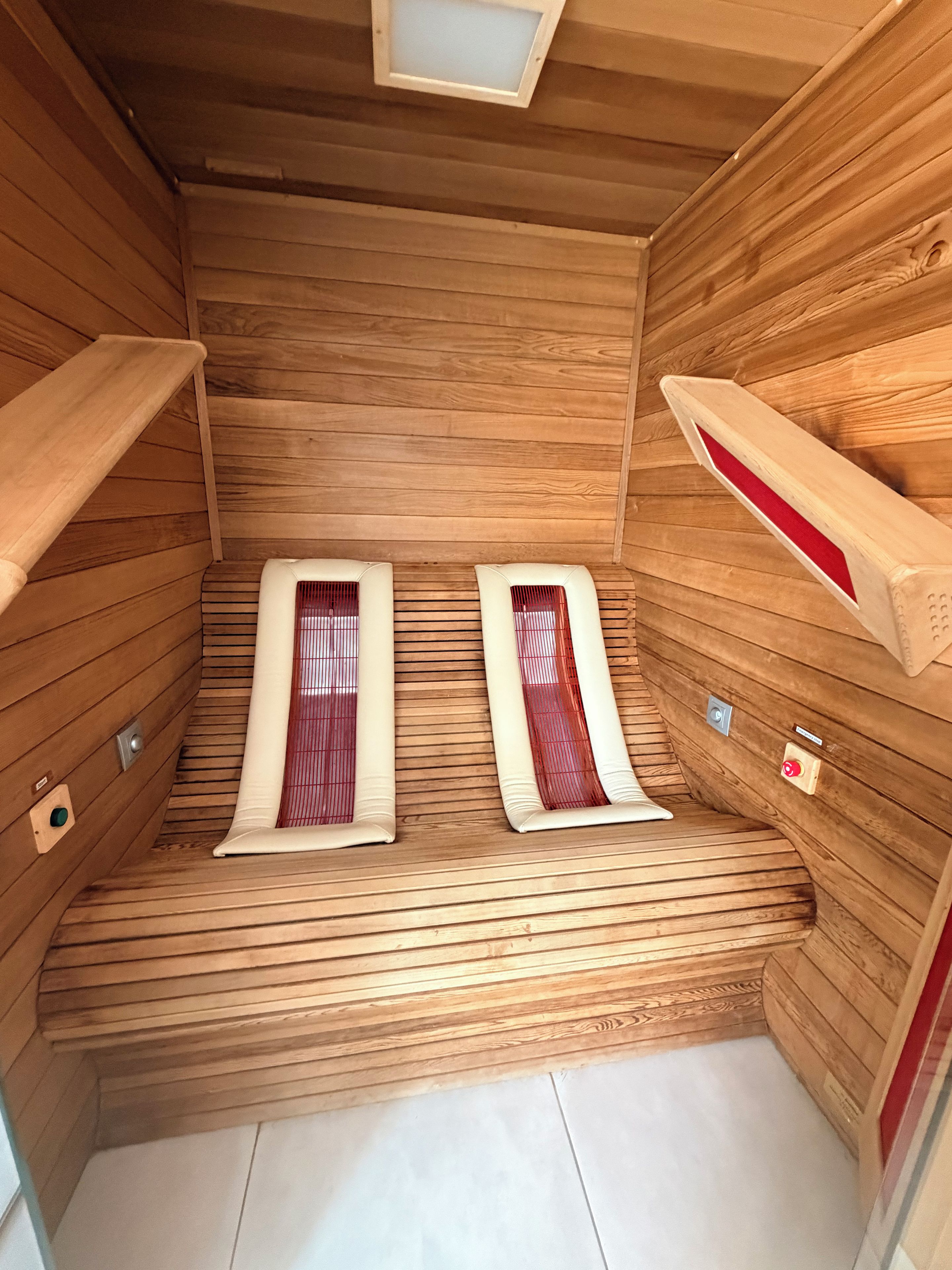 Una sauna amb parets i bancs de fusta, equipada amb panells de control i un sistema de ventilació.