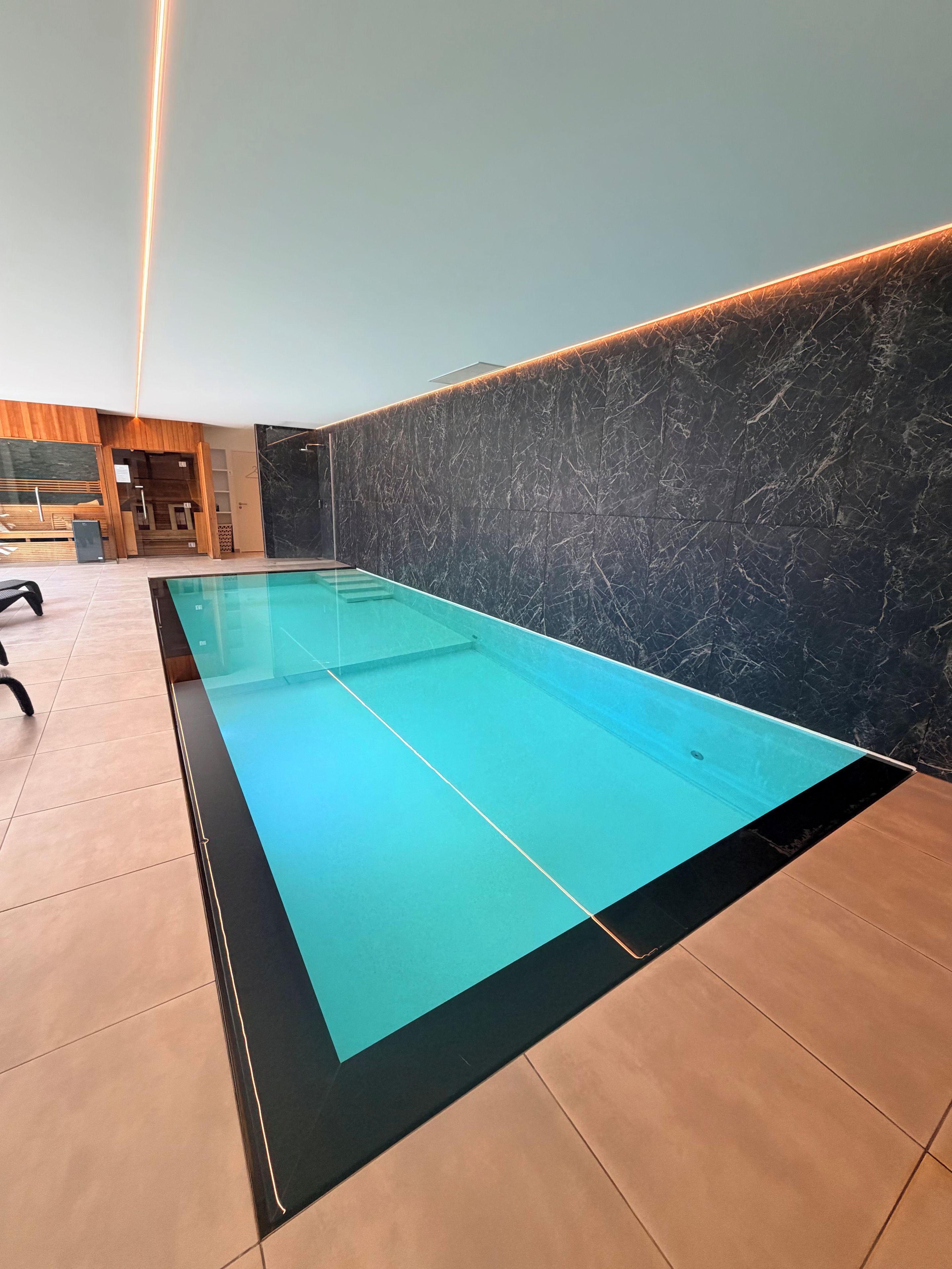 A swimming pool with a black edge and a marble wall.