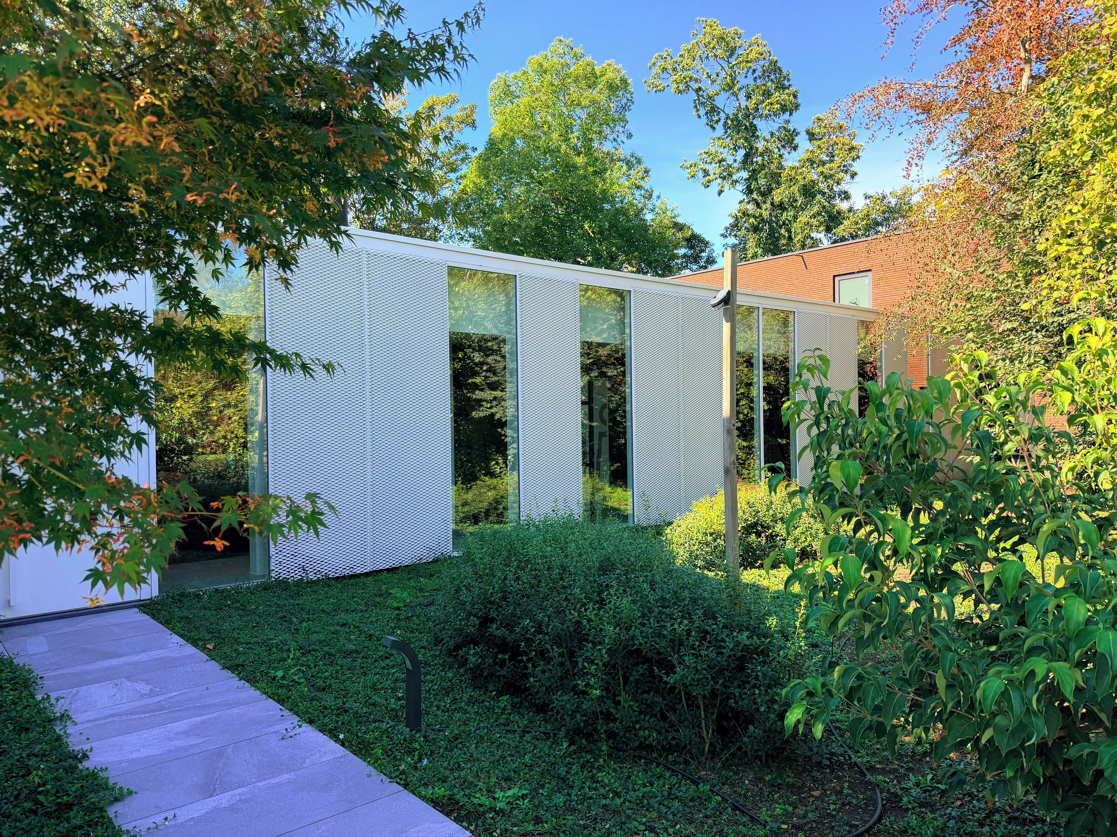 Edifici modern amb façana de vidre, envoltat de vegetació exuberant i un cel clar.