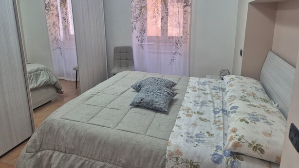 Quarto com cama, cadeira, escrivaninha e janela com cortinas florais.