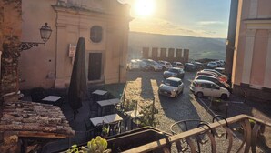 Vista da rua com carros estacionados, um edifício com uma cruz no topo e o sol se pondo ao fundo.
